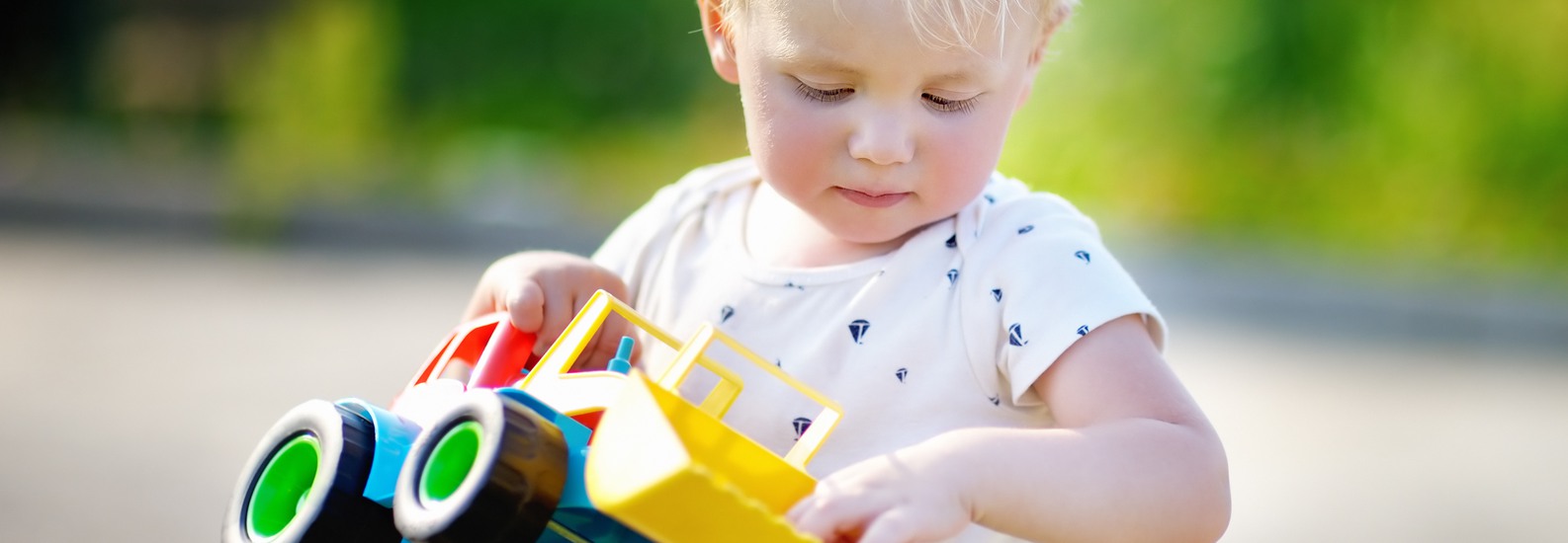 Ett litet barn som leker med en traktor av plast utomhus.