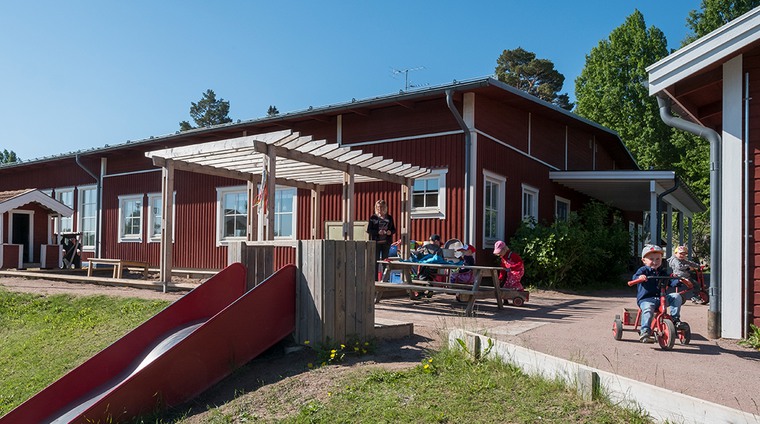 Förskolan i Tällberg och dess förskolegård med rutschkana och lekande barn och en vuxen syns på bilden.