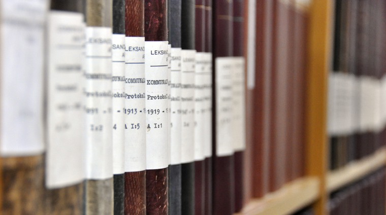 Närbild på en arkivhylla med rader av gamla inbundna böcker med protokoll.