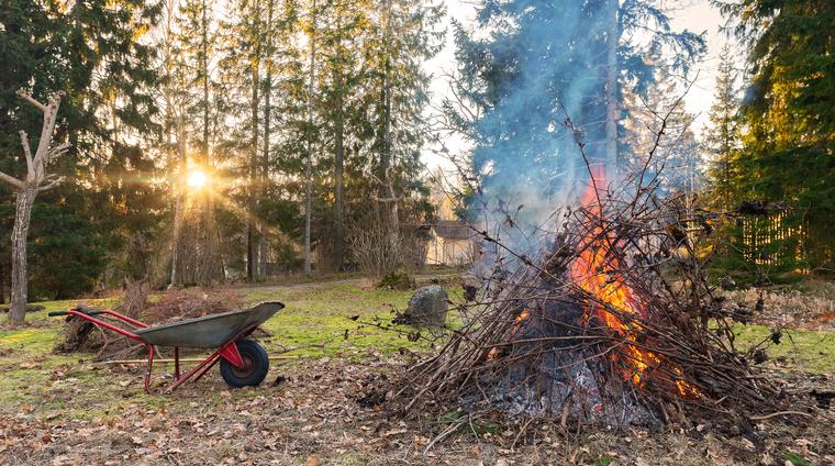 En brinnande brasa med trädgårdsavfall och en skottkärra
